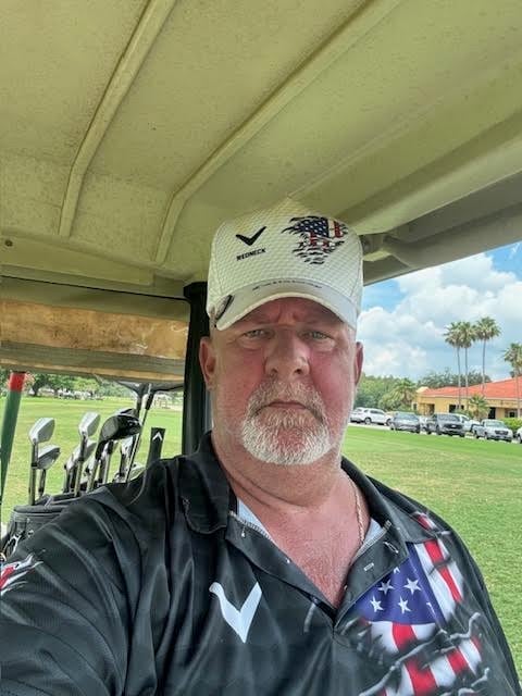 Steve showing his American flag shirt and SV Notaries hat while sitting on a golf cart